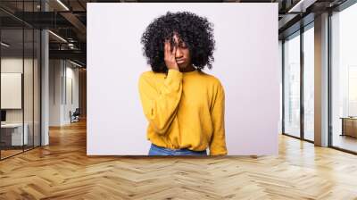 Sad pretty girl feeling upset while spending time at home alone. Beautiful young dark-skinned female with Afro hairstyle staring at camera with unhappy or regretful look against studio wall Wall mural